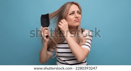 sad upset blond young woman with falling hair combing her hair on a blue background