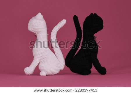 Amigurumi two cats in love sitting on pink background. DIY soft toys made of natural cotton and wool. Crocheted black and white kittens, handmade art. Romantic relationships between pets.