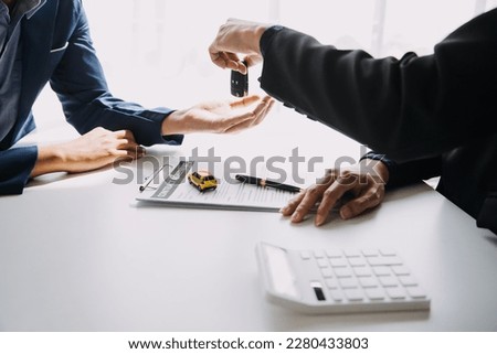 A car rental company employee is handing out the car keys to the renter after discussing the rental details and conditions together with the renter signing a car rental agreement. Concept car rental. Royalty-Free Stock Photo #2280433803
