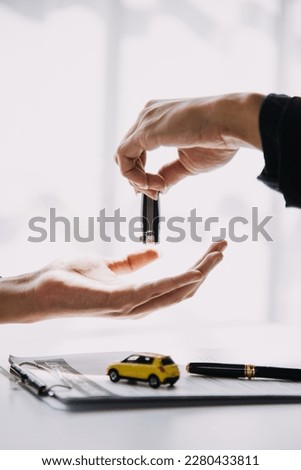 A car rental company employee is handing out the car keys to the renter after discussing the rental details and conditions together with the renter signing a car rental agreement. Concept car rental. Royalty-Free Stock Photo #2280433811