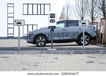 e-car charging station also known as a electric car charge point or electric vehicle supply equipment (EVSE) with information sign electric-car charging on parking spaces and a e-car in the background