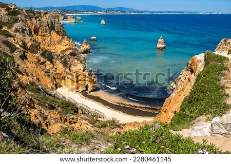 A stunning view of Praia do Camilo beach with its iconic staircase leading down to the Atlantic Ocean, captured from the viewpoint at the top of a nearby cliff with Lagos visible in the background. Royalty-Free Stock Photo #2280461145