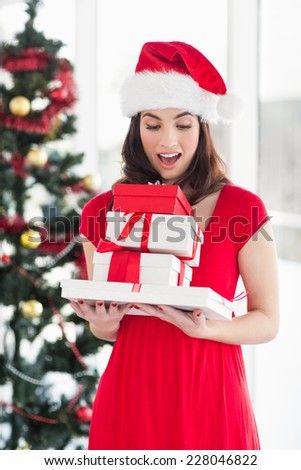 Surprised brunette in red dress holding pile of gift at home in the living room