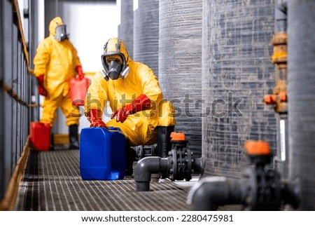 Fully protected workers in yellow hazmat suit, gas masks and gloves handling dangerous chemicals or substances. Royalty-Free Stock Photo #2280475981
