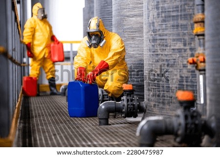 Experienced and protected workers in yellow chemicals suit, gas masks and gloves handling biohazardous waste. Royalty-Free Stock Photo #2280475987