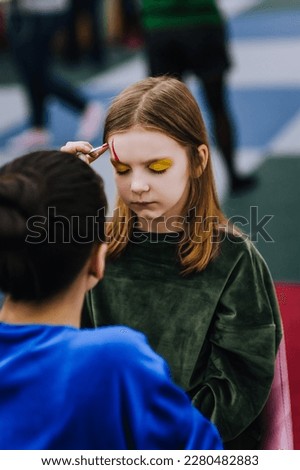 A professional make-up artist, woman artist paints face painting on her face with paints, drawing, children's makeup for a little girl model, a child. Photography, art, concept, lifestyle.