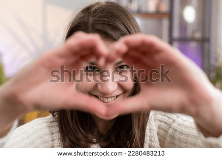 I love you. Happy young woman at home living room couch makes symbol of love, showing heart sign to camera, express romantic feelings express sincere positive feelings. Charity, gratitude, donation