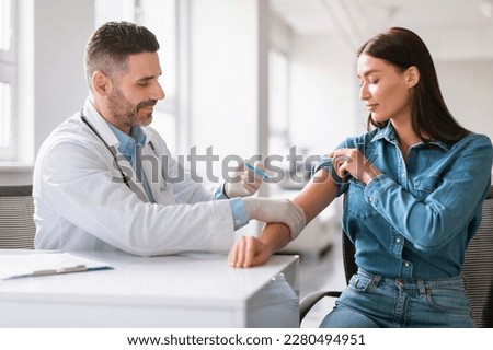 Young european woman getting vaccinated against coronavirus, middle aged male doctor making injection in female shoulder, sitting in clinic interior, copy space Royalty-Free Stock Photo #2280494951