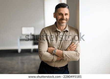 Portrait of confident middle aged businessman in shirt standing in office hall, posing with crossed hands and leaning on wall, looking and smiling at camera, copy space Royalty-Free Stock Photo #2280495181