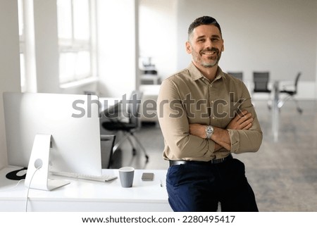 Successful middle aged male entrepreneur sitting with arms crossed at desk in office, looking and smiling at camera, free space. Confident male graphic designer working at company Royalty-Free Stock Photo #2280495417