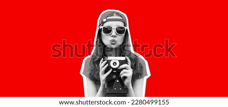 Portrait of happy young woman photographer taking picture on film camera and blowing her lips wearing baseball cap on red background, magazine style