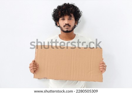 Serious Asian young man activist holds piece of empty cardboard sign in his hands standing on white background