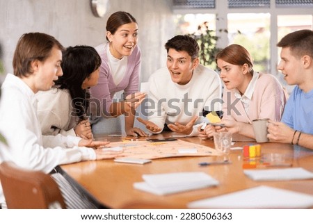 Happy emotional young female student spending free time with friends in campus, playing exciting board game Royalty-Free Stock Photo #2280506363