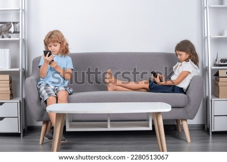 Children alone with phone home. Happy cheerful kids watching media on smartphone, making video call to parent, playing online game, using internet. Parental control, social media addiction. Bad habit.