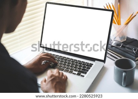 View over man shoulder hands typing on keyboard of laptop computer at  desk. Blank screen for your text or graphic display montage.