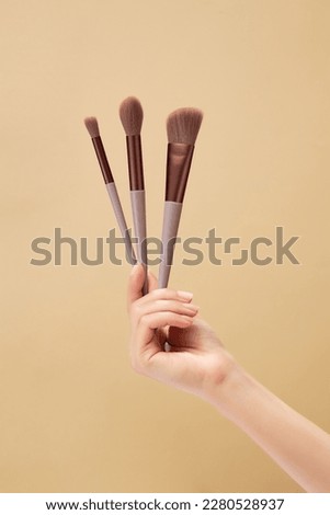 Beautiful female hand holding a set of makeup brushes on a minimal beige background. View from front. Makeup brush branding mockup Royalty-Free Stock Photo #2280528937