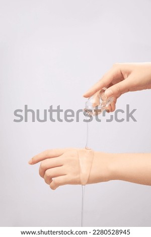 Female hand pouring transparent essence on back of other hand on white background. Beauty cosmetic product for skin care concept. Mockup for package design Royalty-Free Stock Photo #2280528945