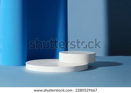 Two empty round white platforms stacked on top of each other, decorated on blue background. Empty space for display product, text and design. Royalty-Free Stock Photo #2280529667