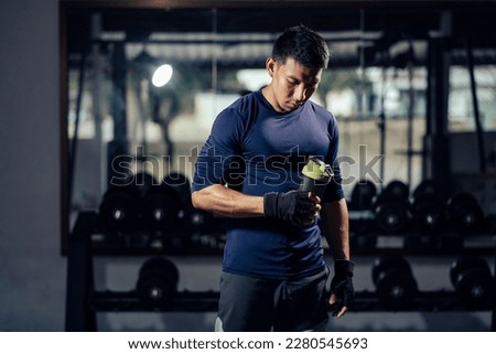 Fitness man in sportswear holding a bottle water or protein shake for drink in fitness gym. Health care and workout. Asian man replenishing water balance after workout. Concept of health and wellness. Royalty-Free Stock Photo #2280545693