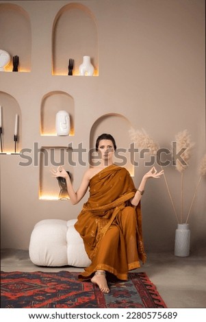 a beautiful young woman in a traditional Indian dress is sitting on a soft pouf in the studio. selective focus