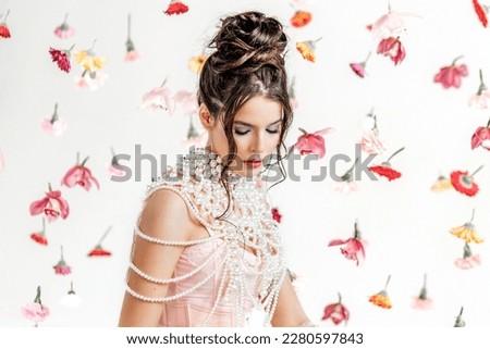 An attractive young woman in a pink short dress in a light spring studio with floating flowers. Beauty and fashion.