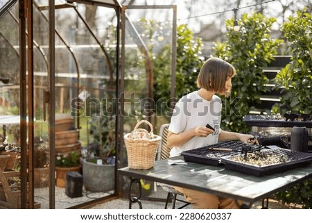 Young gardener signs the names of the plants that she plants into seedling trays in garden. Concept of hobby or small business of growing flowers