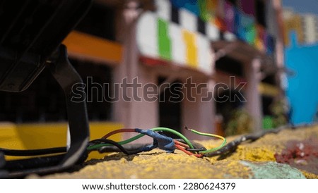 A bunch of colorful wires in the foreground over a yellow wall with a colorful building in the background out of focus