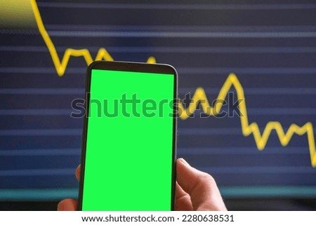 Black phone with blank mockup screen on rising stock graph. Closeup hand showing smartphone isolated green display. Online banking, Fund App use. Financial analyst on Invest Market. Bank collapse 2023