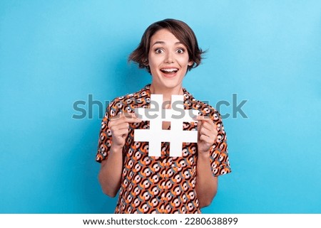 Photo of cheerful excited woman wear print blouse smiling holding hashtag card open mouth isolated blue color background