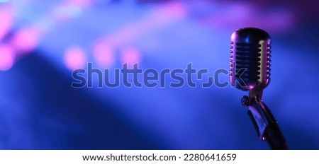 
Vintage vocal microphone in the dark on a concert stage with pink and blue spot lighting. Live music or podcast wide banner background with copy space Royalty-Free Stock Photo #2280641659