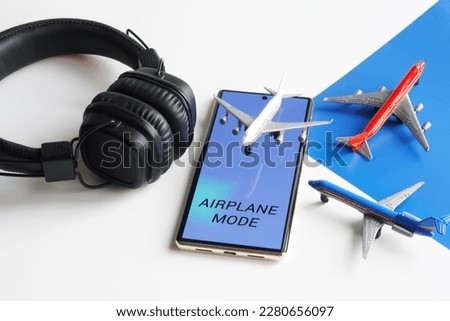 Mobile phone - smartphone with "Airplane mode" enabled and toy passenger airliners on white and blue. Concept of disabling communication functions of gadgets during an airplane flight. Close-up Royalty-Free Stock Photo #2280656097