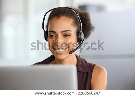 Call center agent with headset working on support hotline in office. Black businesswoman in conversation with customer during video call. African american business woman working remotely on laptop. Royalty-Free Stock Photo #2280660247