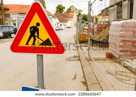 Red triangle traffic sign for road works and blue signpost for indicate blind road installed on the roadway in front of the fenced construction site. Building with scaffold is under construction. Royalty-Free Stock Photo #2280660647