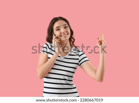 Young woman talking by smartphone and pointing at something on pink background