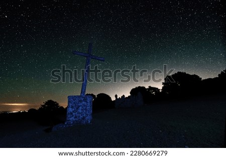 Long Exposure night photograph with stars in the background and foreground a cross and trees