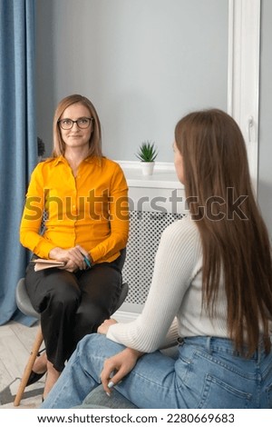 Happy woman psychologist with glasses looks into the camera, consulting a young woman in the office interior. Therapy, mental problems, psychological support and professional help. Vertical photo