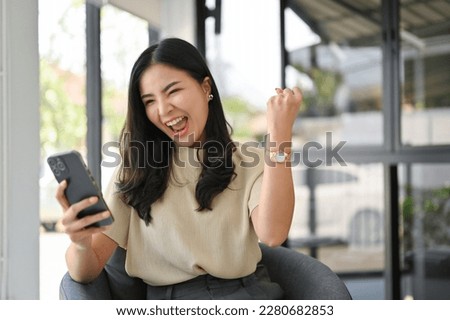 Overjoyed and excited millennial Asian woman screaming with joy, looking at her phone screen, rejoicing, receiving good news, winning lottery. Royalty-Free Stock Photo #2280682853