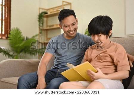 Happy and caring Asian dad is teaching his son to read a book, telling a fairytale story, or reading a cartoon together on a sofa in the living room. happy family
