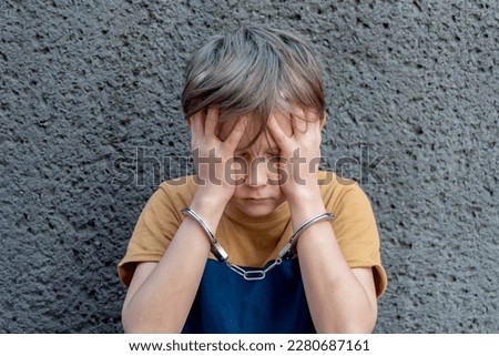 A 10-year-old criminal, handcuffed against a gray wall. Concept: juvenile delinquency, petty theft and theft, incarceration. Royalty-Free Stock Photo #2280687161
