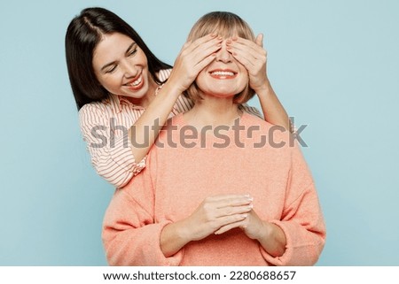 Fun elder parent mom with young adult daughter two women together wear casual clothes close eyes with hands play guess who or hide and seek isolated on plain blue cyan background. Family day concept