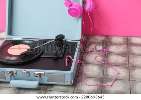 Record player with vinyl disk and headphones on table near pink wall, closeup
