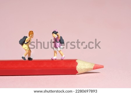 Miniature tiny people toys photography. Two kids standing above red pencil. Isolated on pink background. Image photo