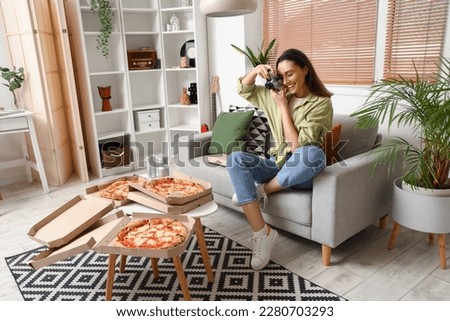 Beautiful woman with camera taking picture of tasty pizza at home