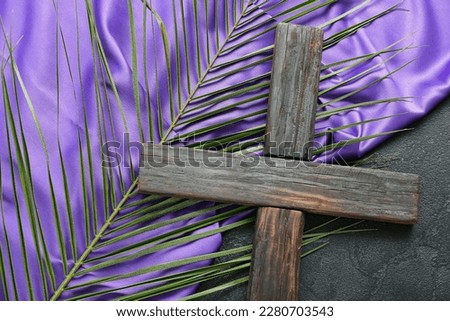 Wooden cross with palm leaf and purple fabric on dark background, closeup. Good Friday concept