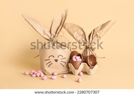 Easter bunny gift bag, holder with chocolate eggs and candies on beige background Royalty-Free Stock Photo #2280707307