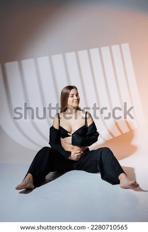 Smiling pregnant woman in a black suit on a gray background. Beautiful elegant pregnant woman.