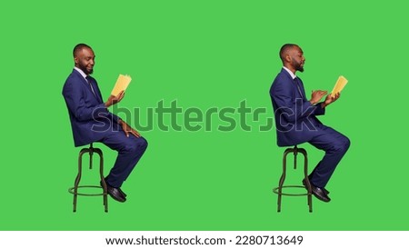 Young businessman sitting on chair reading story book or novel, being focused on fictional tale for leisure activity. Confident entrepreneur reading literature over full body green screen.