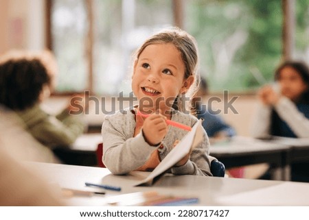 Happy little girl learning to draw with a colour pencil in an elementary art class. Primary school kid talking to her teacher as she receives quality education in a positive learning environment. Royalty-Free Stock Photo #2280717427