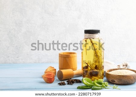 Sunflower oil in a glass jar with various herbs and spices, sesame, rosemary, star anise, basil on a blue wooden background. Side view, copy space.