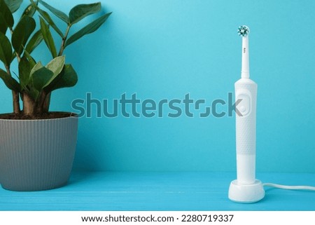Electric toothbrush with green flower on blue background. Top view